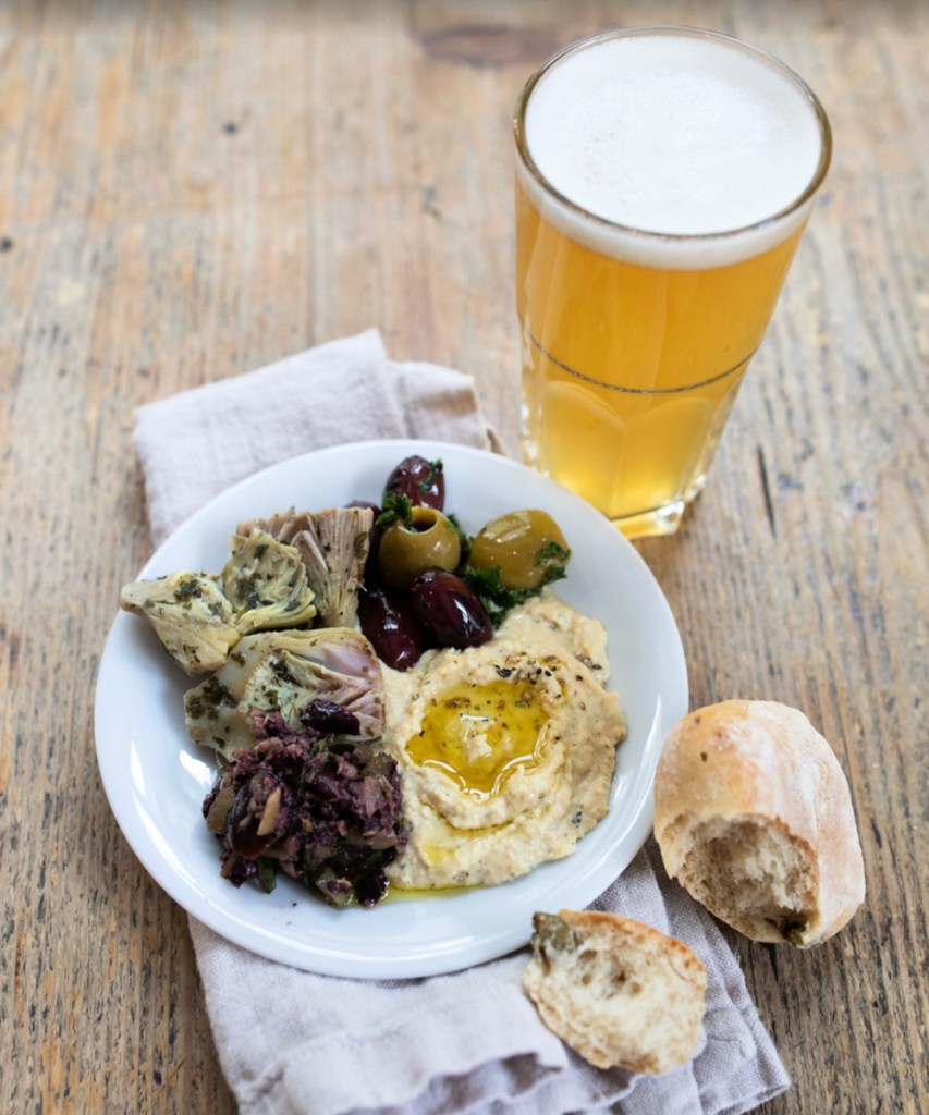 A plate of olives, artichokes and hummus and a glass of beer at a vegetarian restaurant.