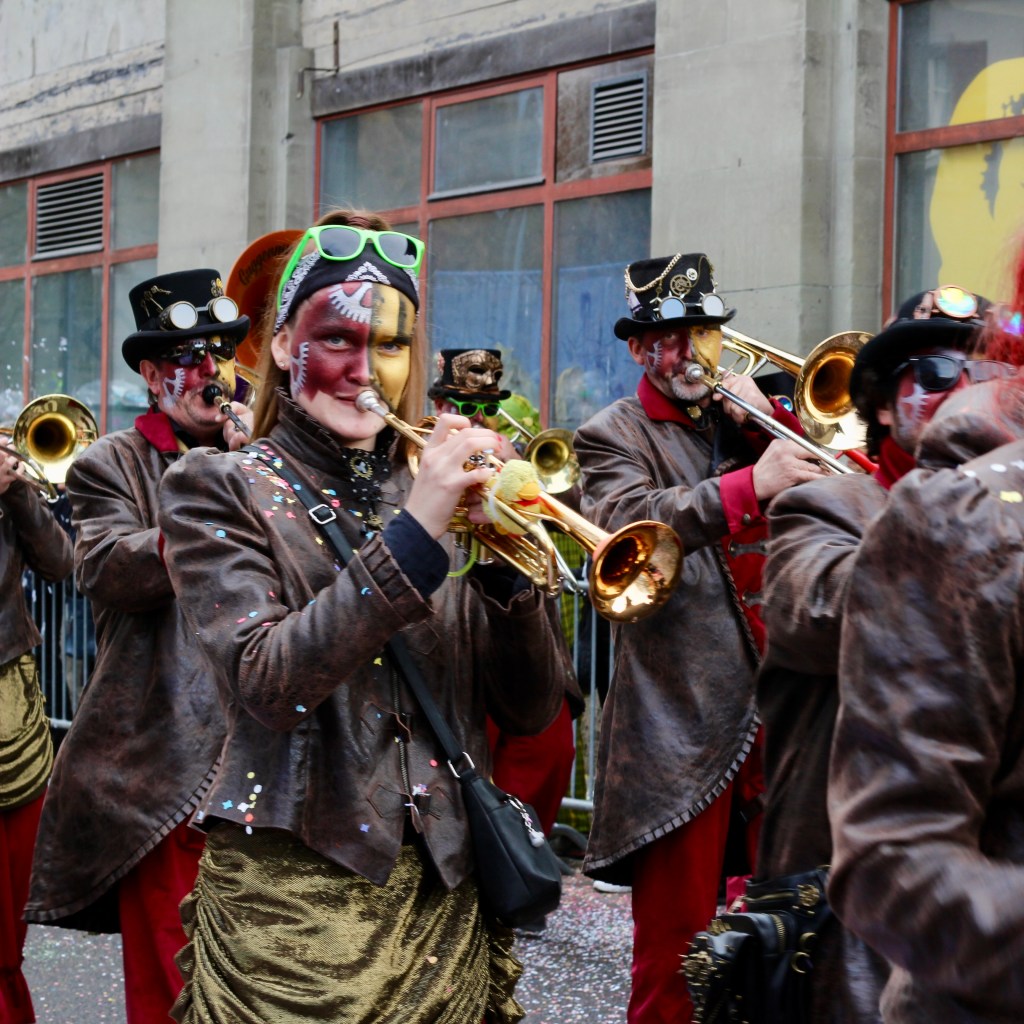 A woman with a painted face plays the trumpet in the parade.
