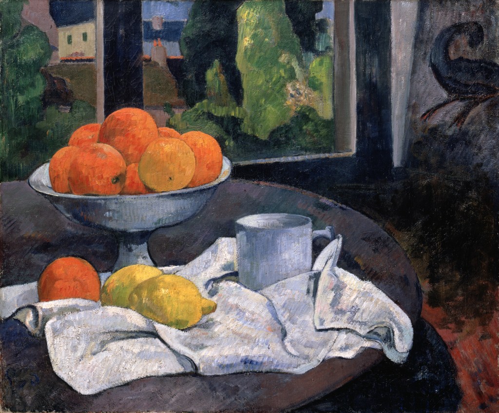 A bowl of oranges and lemons sit on a white tablecloth, on a table set before a window with nature scene outside. 